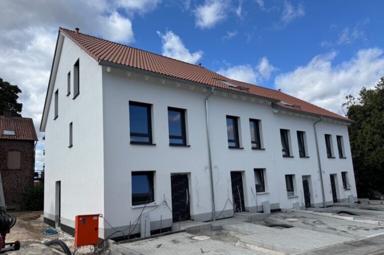 Mehrfamilienhaus im Bau mit weißer Fassade und rotem Ziegeldach bei bewölktem Himmel